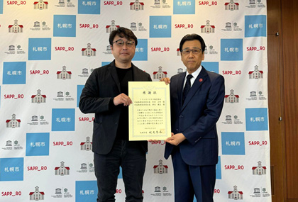 transcosmos receives a certificate of appreciation from the Mayor of Sapporo Right: Katsuhiro Akimoto, Mayor of Sapporo city Left: Satoshi Takayama, Corporate Executive Officer, Division Manager of Government Relations & Public Affairs, transcosmos