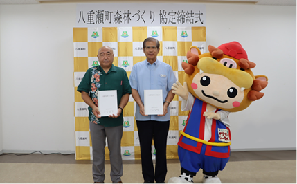 At the ceremony from left: Hirofumi Inoue, Corporate Senior Officer at transcosmos inc.; Yasuhiro Arakaki, Mayor of Yaese-cho; Shi-chan, an official mascot of Yaese-cho