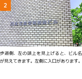 2　歩道側、左の頭上を見上げると、ビル名が見えてきます。左側に入口があります。